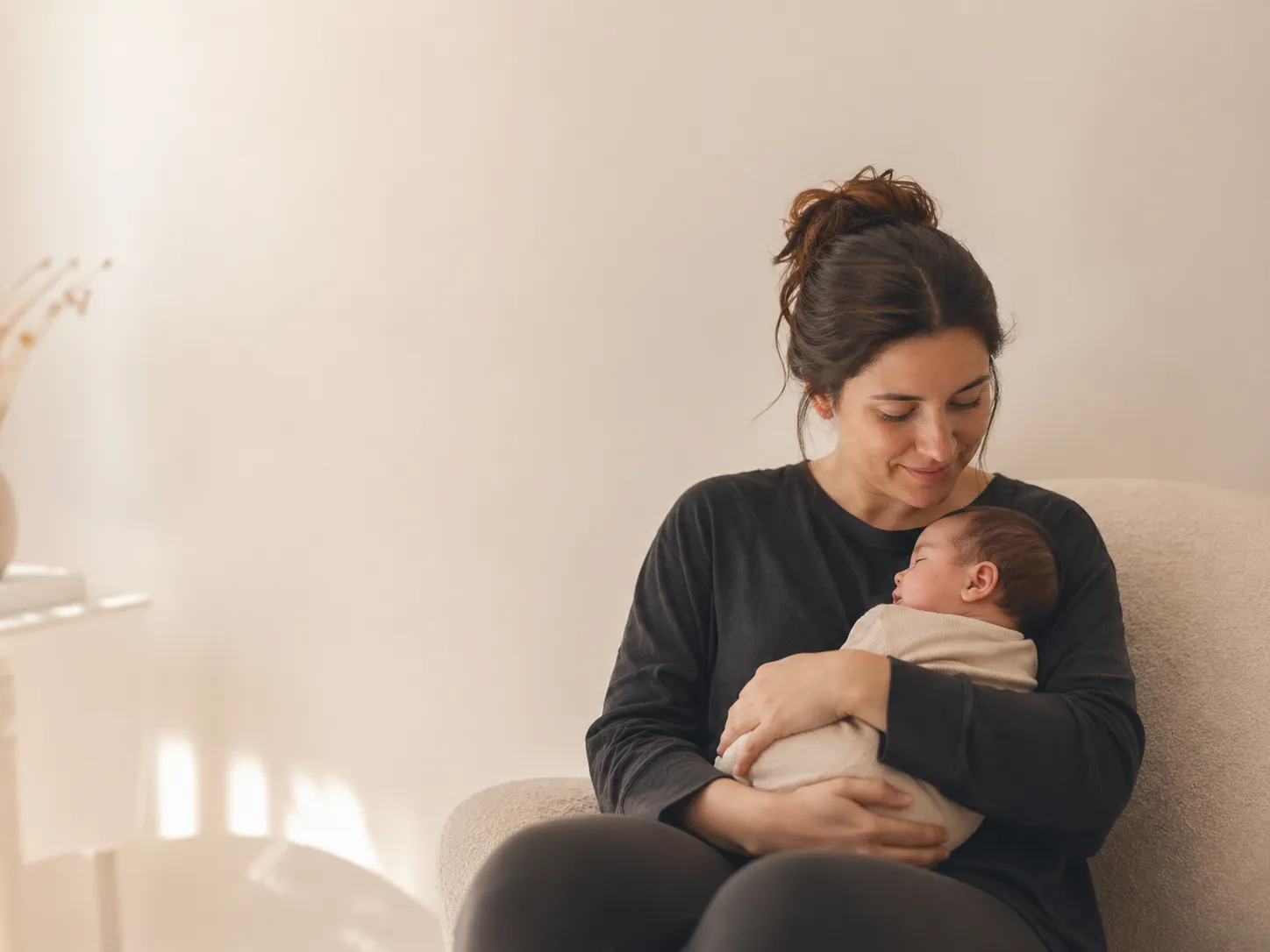 A young mother holding a sleeping baby in soft light.